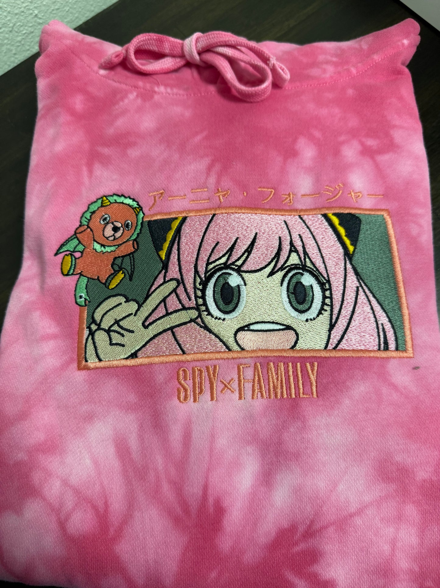A pink tie-dye hoodie with a graphic print of a character from the anime SPY x FAMILY.